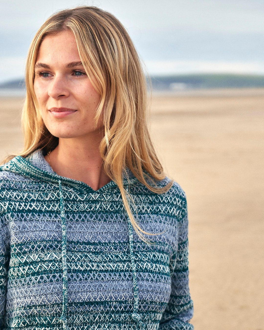 A woman wearing an Erin - Womens Hooded Knit - Light Green sweater on the beach by Saltrock.