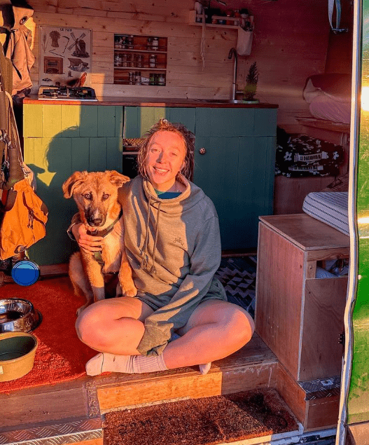 A woman smiling with her dog inside a cozy, sunlit camper van, surrounded by Saltrock Harper Womens Longline Pop Sweat in Green cabinets and outdoor gear embroidered branding.