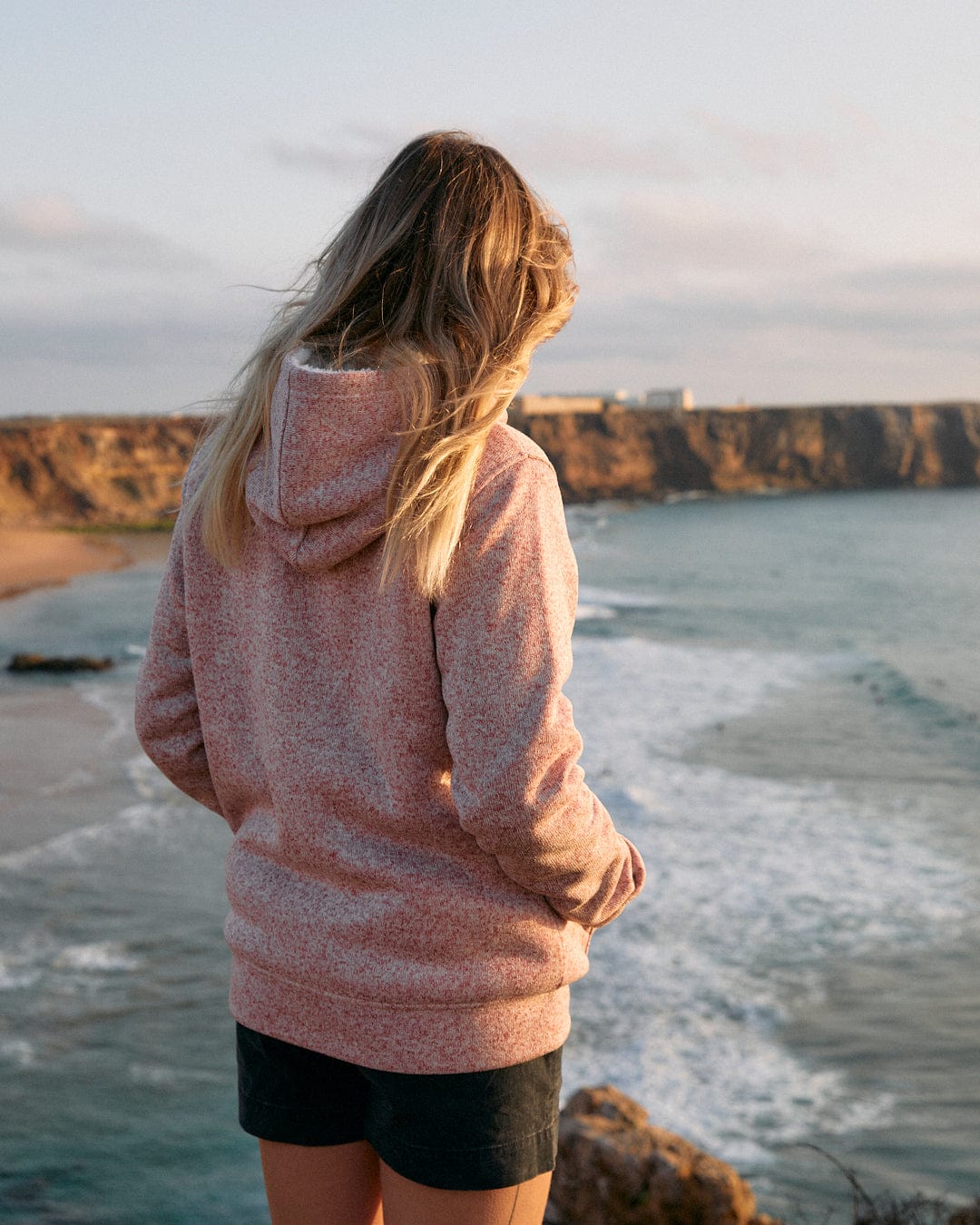A woman in a Farley - Womens Borg Lined Hoodie in Pink by Saltrock gazes at the ocean.