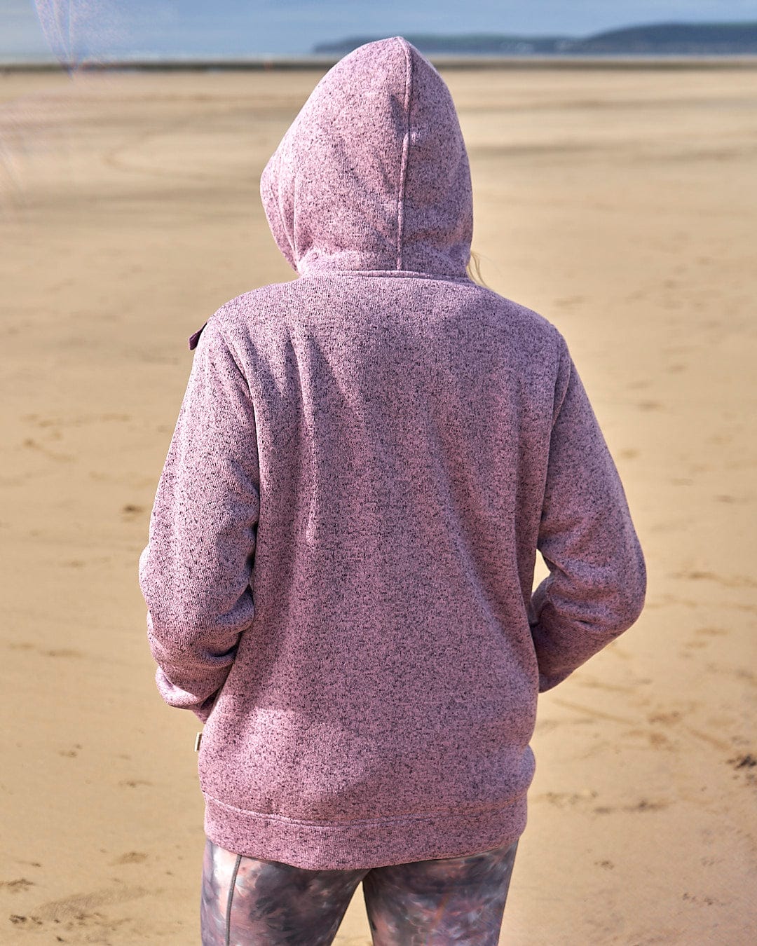 A woman wearing a Saltrock Farley - Lined Zip Hoodie - Purple standing on a beach.