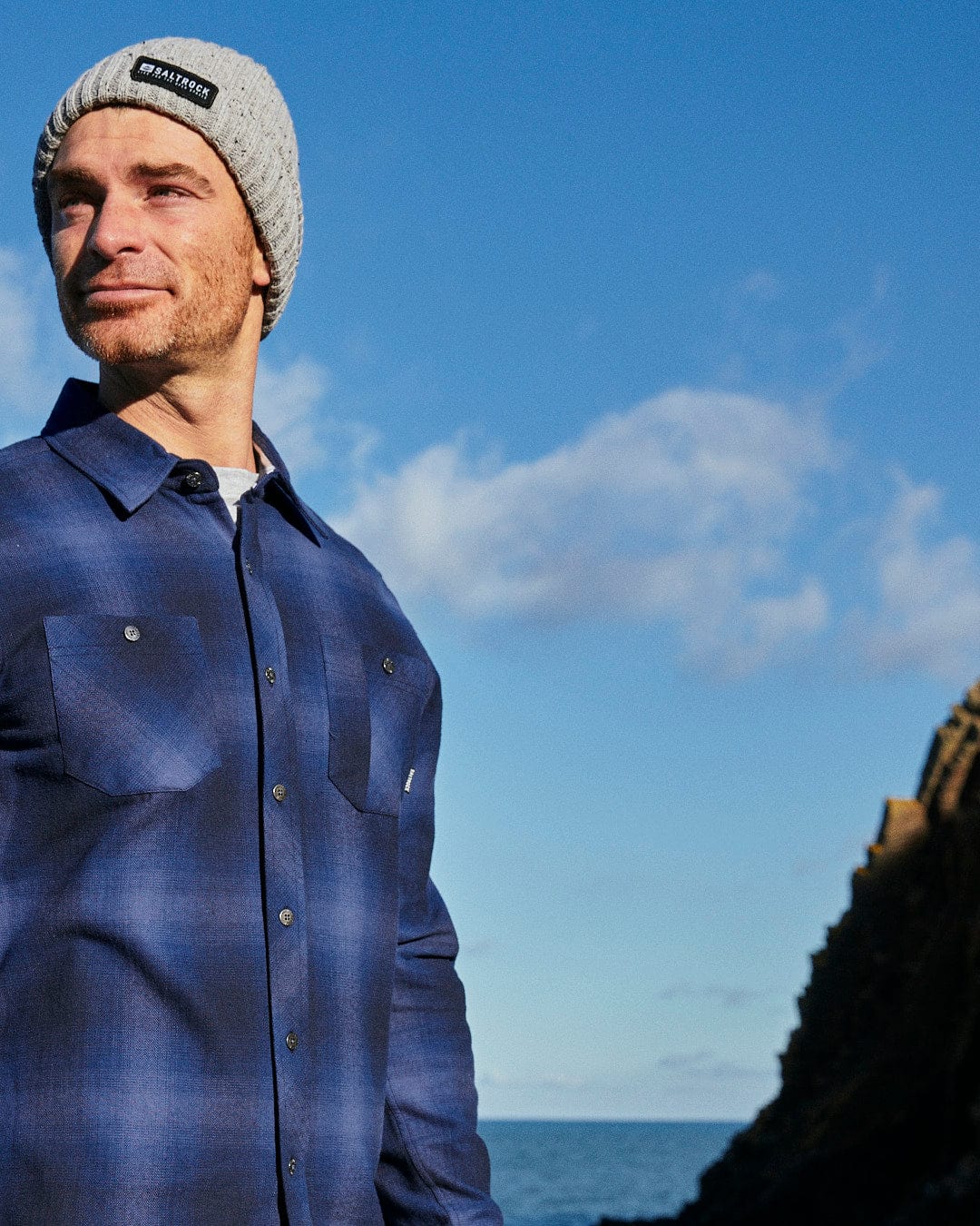 A man in a Farris - Mens Check Shirt - Blue by Saltrock standing by the ocean.