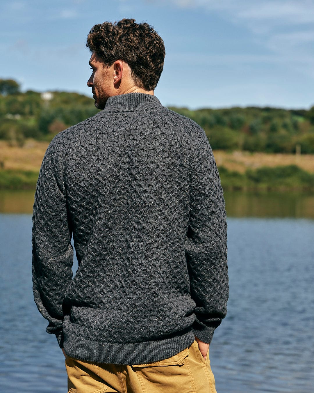 A man is standing by a lake wearing a Saltrock Flint - Mens 1/4 Neck Zip Knit - Black sweater.