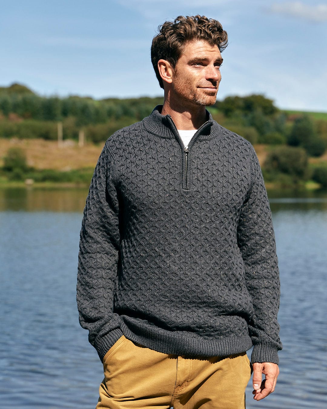 A man is standing next to a lake wearing a Saltrock Flint - Mens 1/4 Neck Zip Knit - Black sweater.