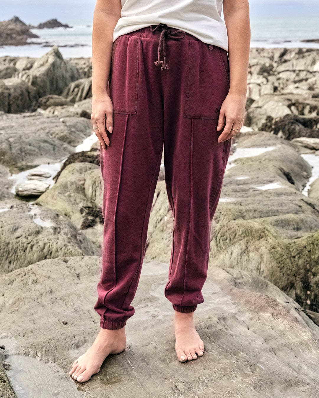 A Saltrock jogger in purple sweatpants standing on rocks by the ocean.
