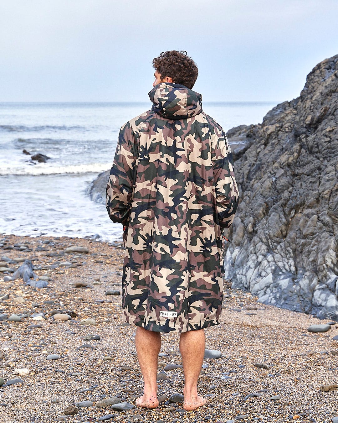 A man in a Saltrock camouflage coat standing on a beach.
