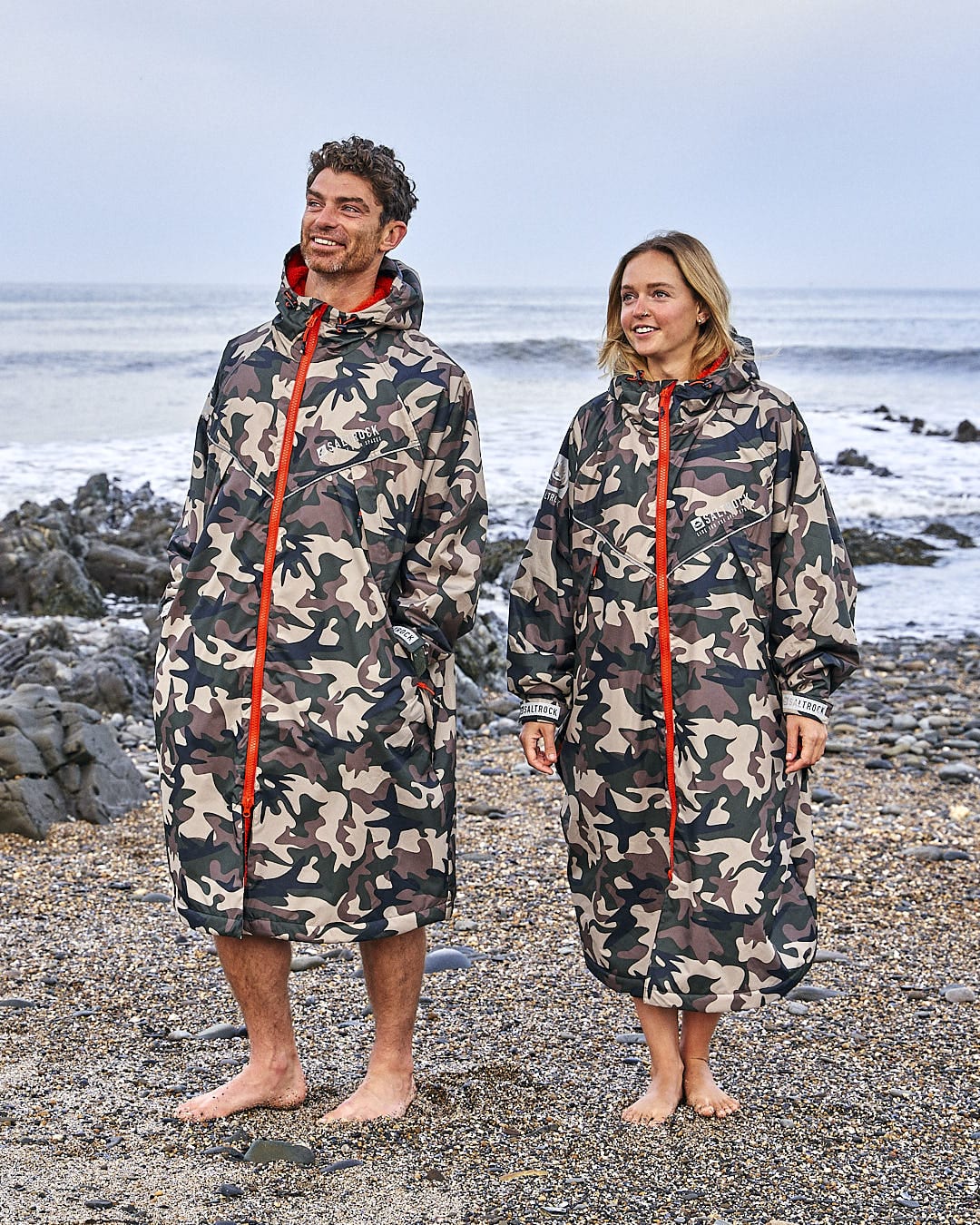 Two people standing on a beach wearing Saltrock's Four Seasons - Waterproof Changing Robe in Brown.
