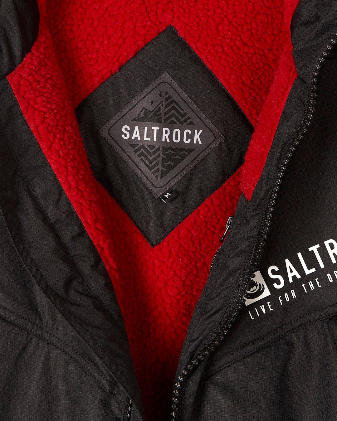 Close-up of a black Saltrock Recycled Changing Robe - Black/Red with an open zipper, revealing a red fleece interior. The interior label proudly displays the Saltrock logo, denoting the brand's commitment to quality and style.