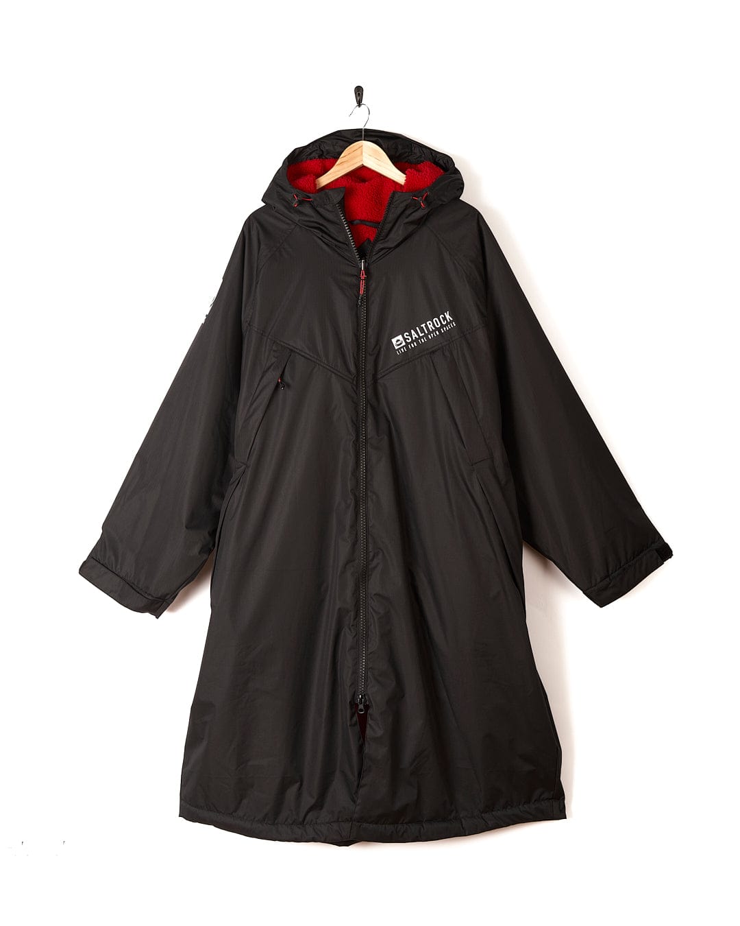 A long black hooded coat with red lining, made from recycled materials, hanging on a wooden hanger. It features a zippered front and a "Saltrock Recycled Changing Robe - Black/Red" logo on the chest.