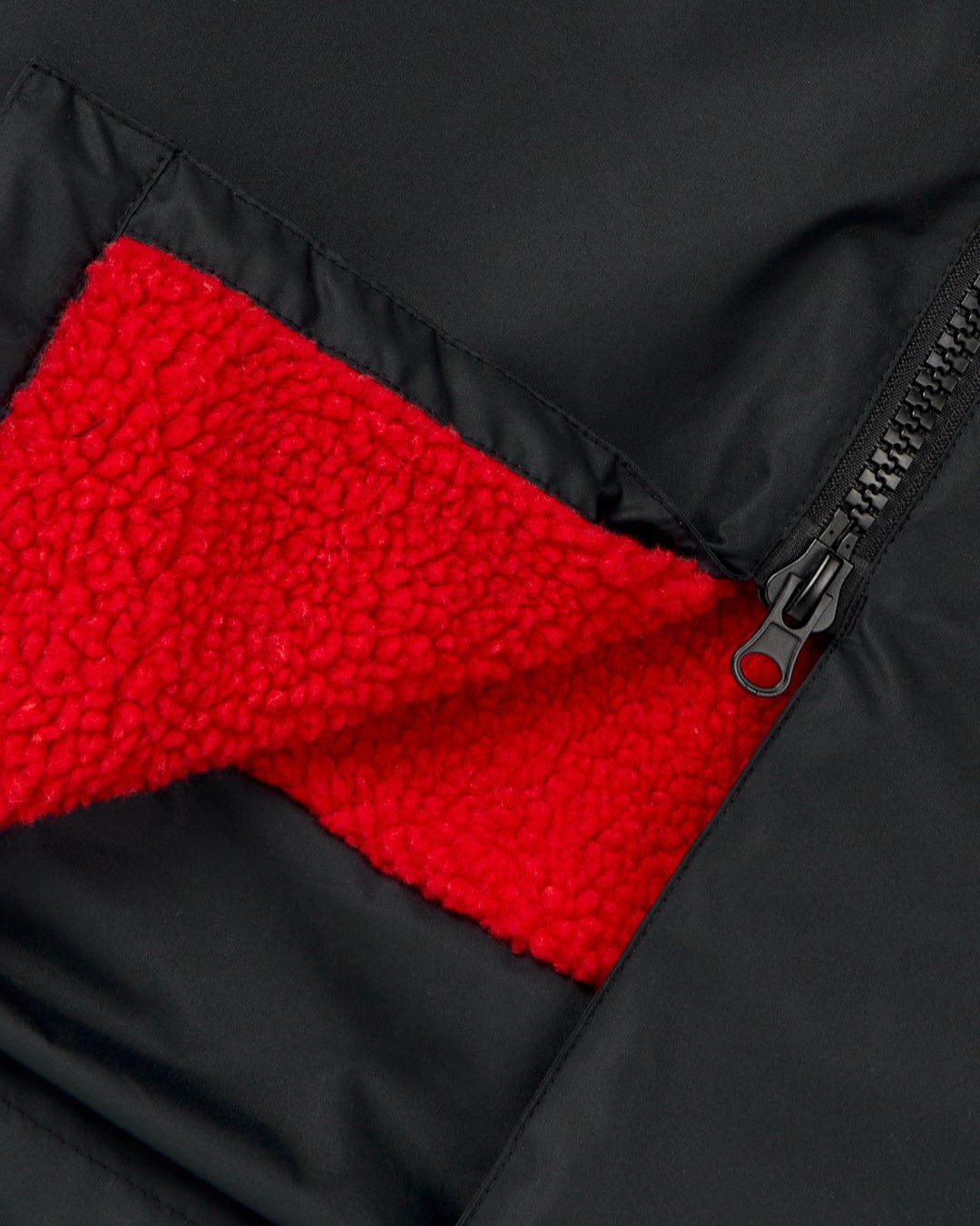 Close-up of a Saltrock Recycled Kids Four Seasons Changing Robe in Black/Red with a red fleece-lined pocket partially unzipped, displaying the textured interior made from recycled material.