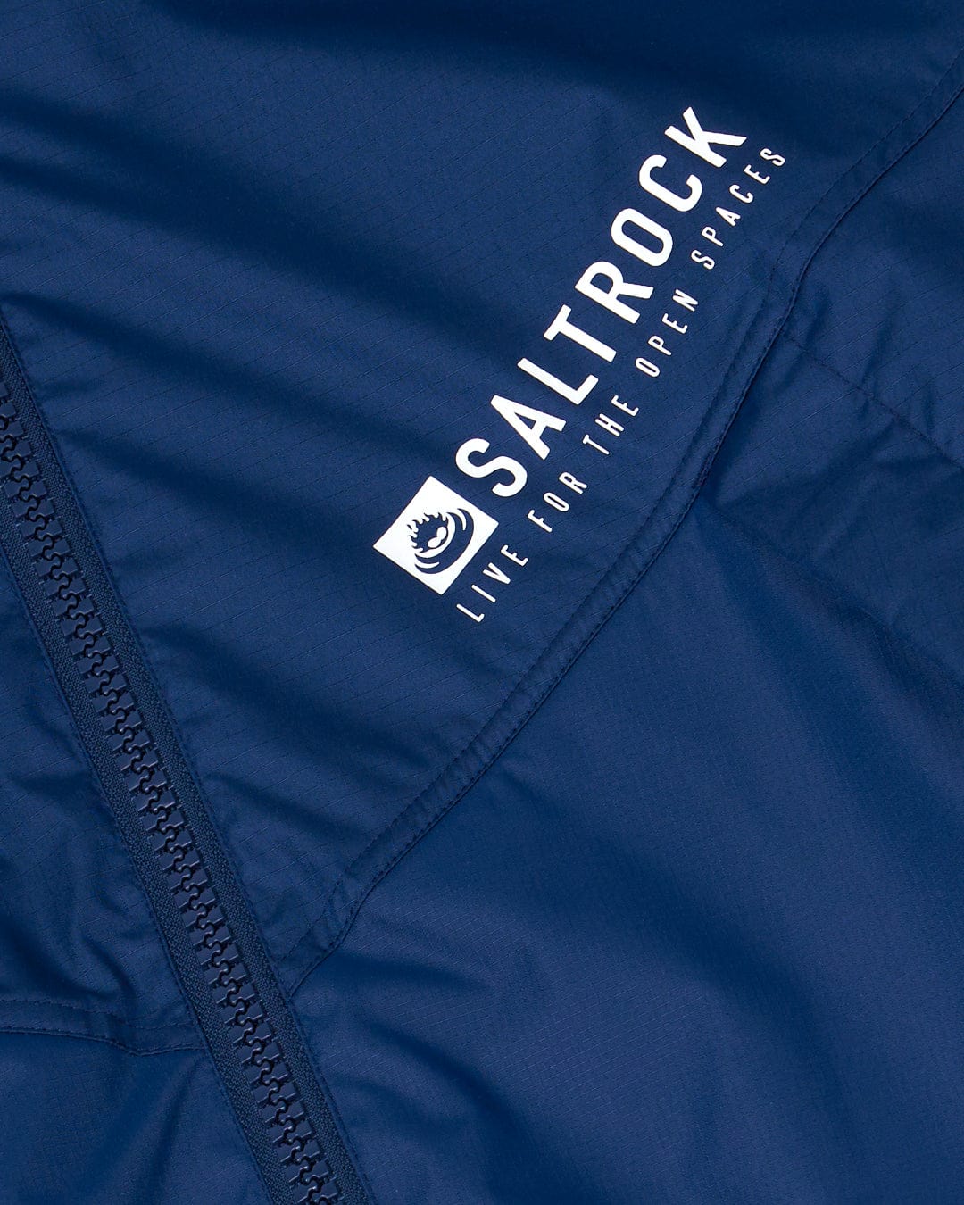 Close-up of a navy blue fabric featuring the Saltrock logo and tagline "Live for the open spaces," with a partially visible zipper on the left side, resembling the detailing found on their popular Changing Robe - Blue.