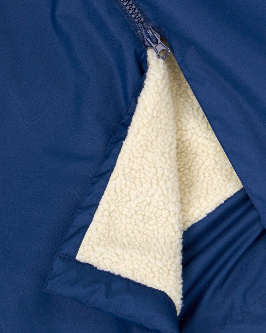 A partially unzipped Saltrock blue jacket revealing a white fleece lining made from recycled material.