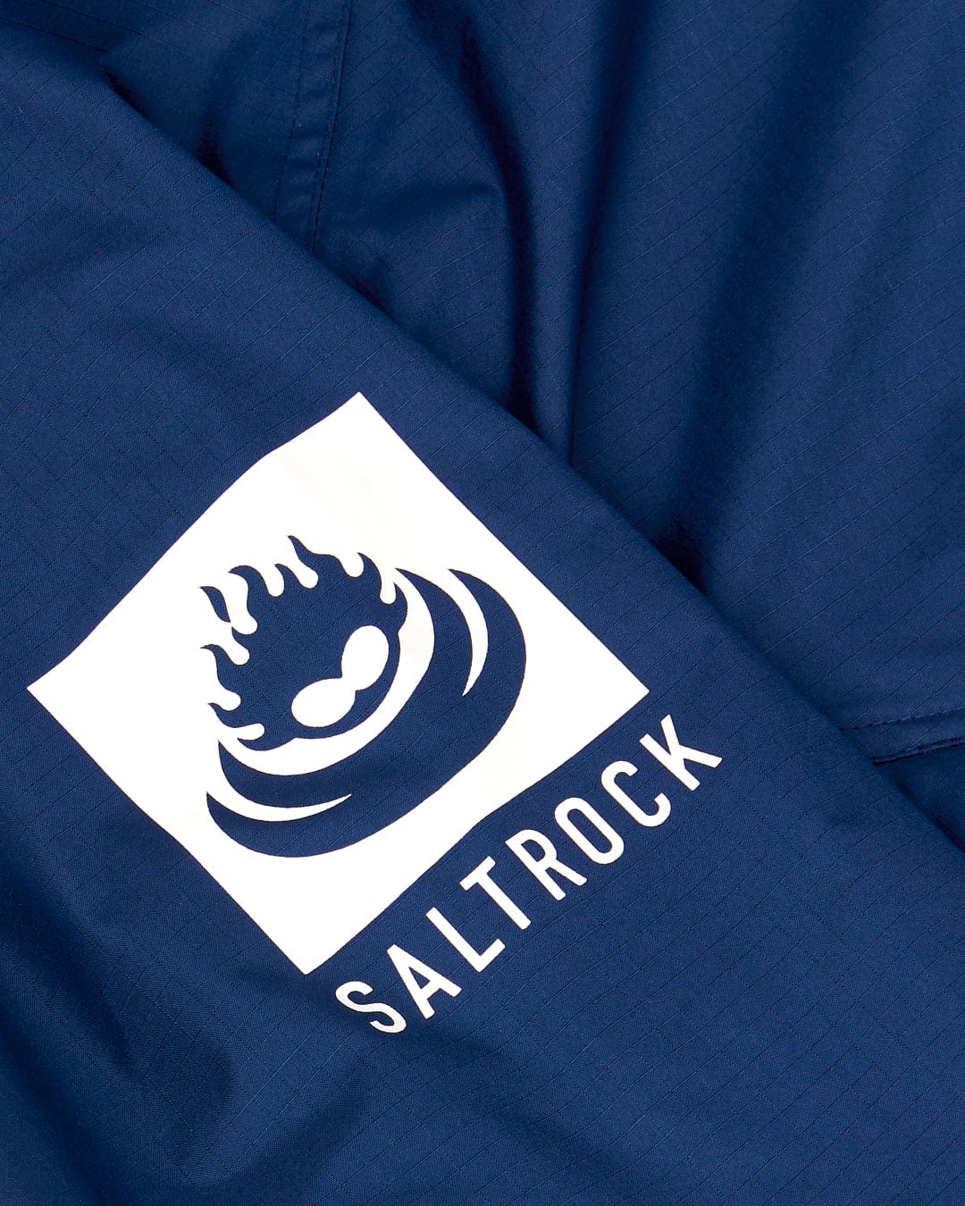 Close-up of a blue Recycled Four Seasons changing robe featuring the Saltrock logo with a stylized flame and wave design in white.