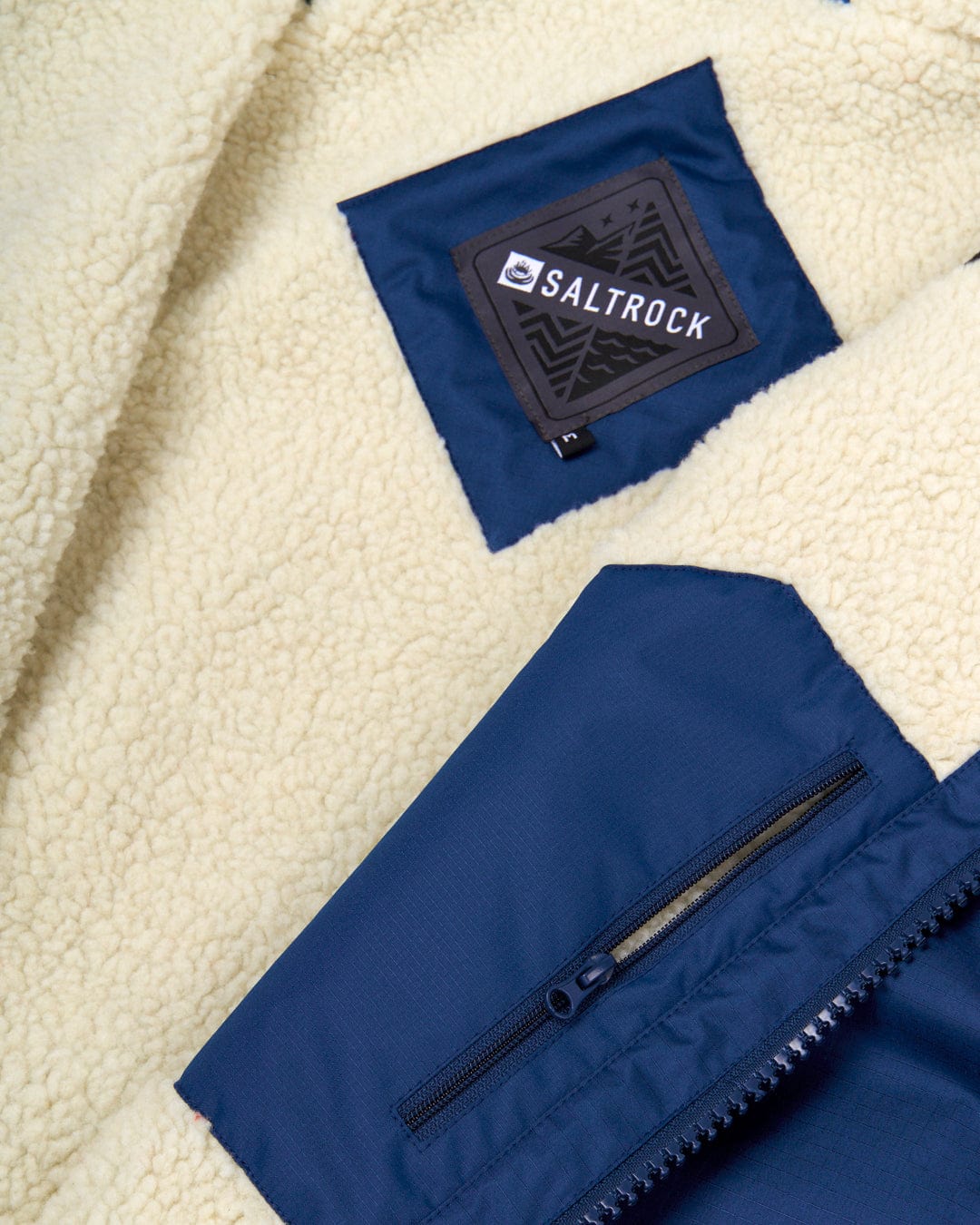 Close-up view of a navy blue Saltrock jacket with a fleece lining, featuring a visible logo patch and zipper detail, redesigned as a waterproof Recycled Four Seasons Changing Robe - Blue.