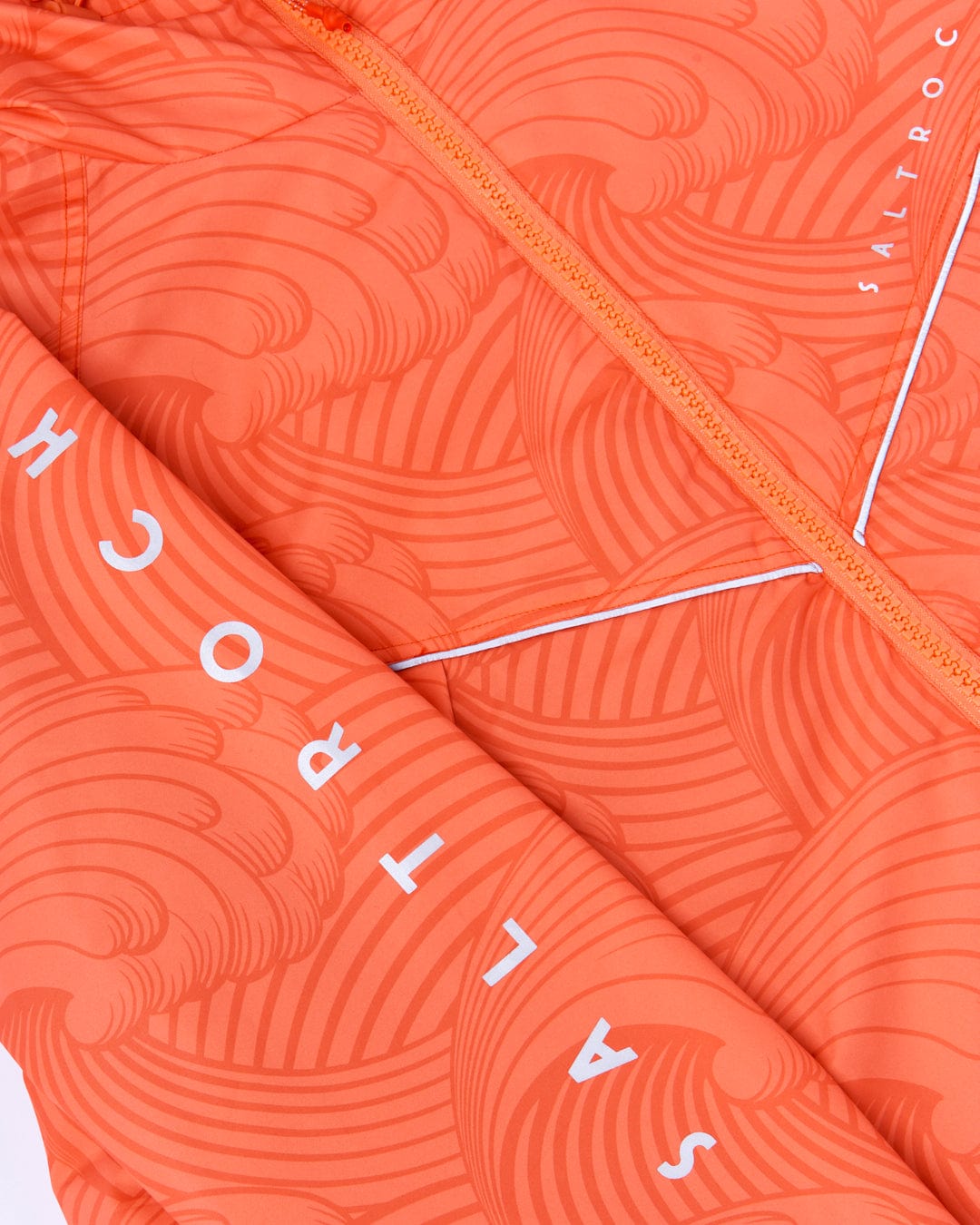 Close-up view of a bright orange textured fabric with a pattern, featuring the word "saltycrew" integrated into the design, crafted from Saltrock's Recycled Four Seasons Changing Robe in Light Orange.