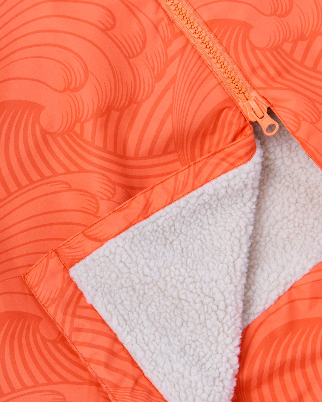 Close-up of a Saltrock Recycled Four Seasons Changing Robe - Light Orange with a white fleece lining and a partially unzipped gold zipper, featuring 3K waterproof ripstop fabric.