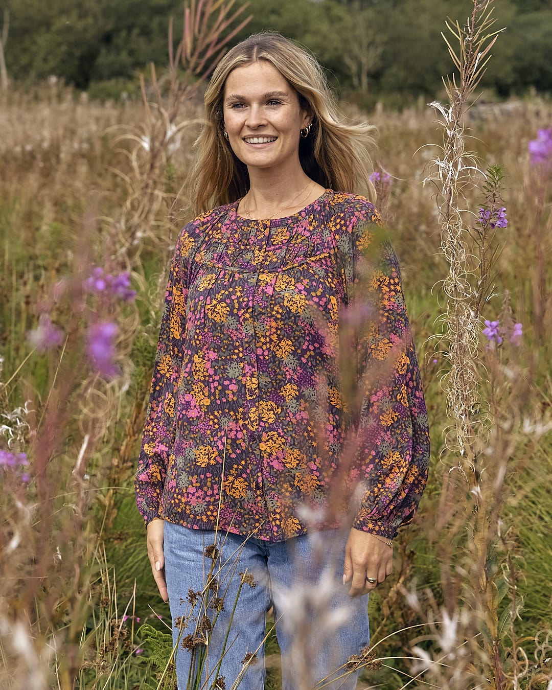 A woman standing in a field of tall grass wearing a Saltrock Garnet - All Over Print Blouse - Orange.