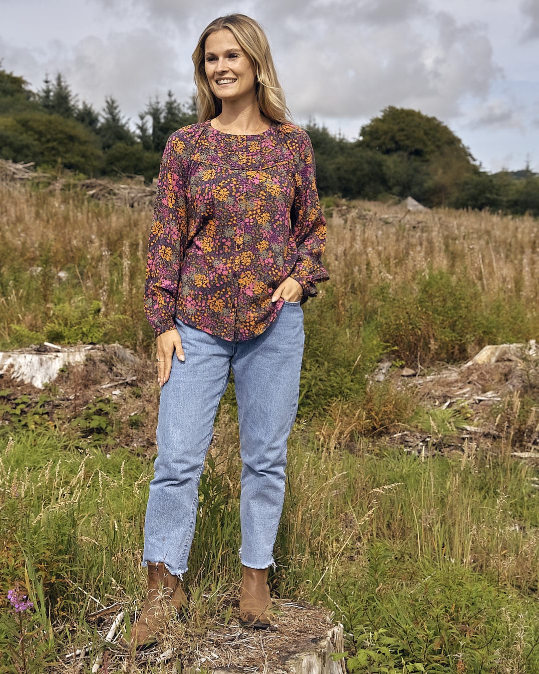 A woman standing in a field wearing Garnet - All Over Print Blouse - Orange by Saltrock, jeans.