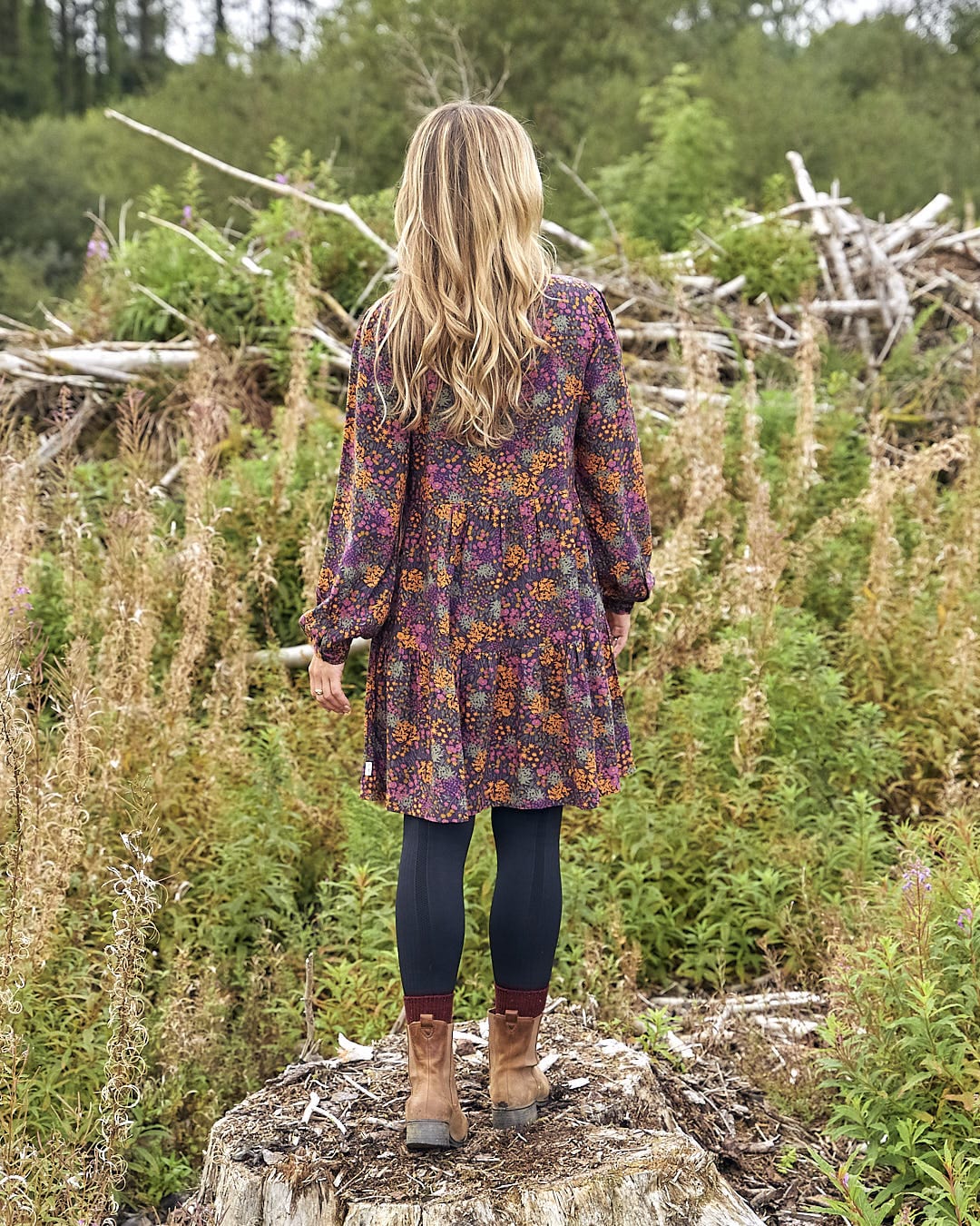 The Saltrock Garnet - Women's Short Dress - Orange, worn by a woman standing on a stump in a field.