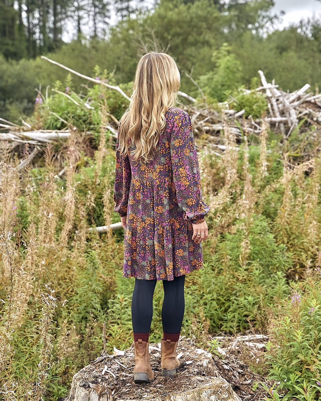 A woman standing on a rock in a field wearing the Saltrock Garnet - Womens Short Dress - Orange.