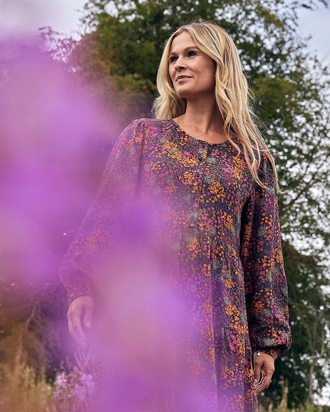 A woman in a floral dress standing in a field wearing the Garnet - Womens Short Dress - Orange by Saltrock.