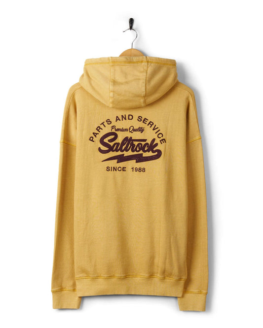 Yellow Saltrock Gas Station hoodie with "saltrock since 1988" text on the back and a kangaroo pocket, hanging against a white wall.