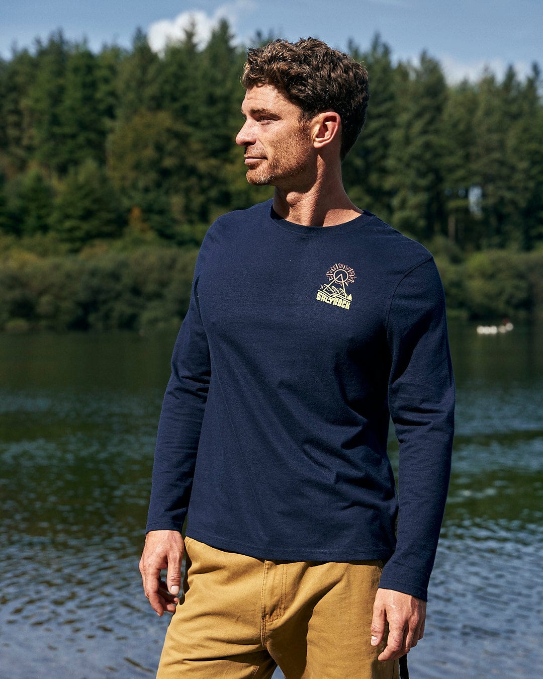 A man wearing a Saltrock Geo Peak - Mens Long Sleeve T-Shirt - Dark Blue standing by a lake.
