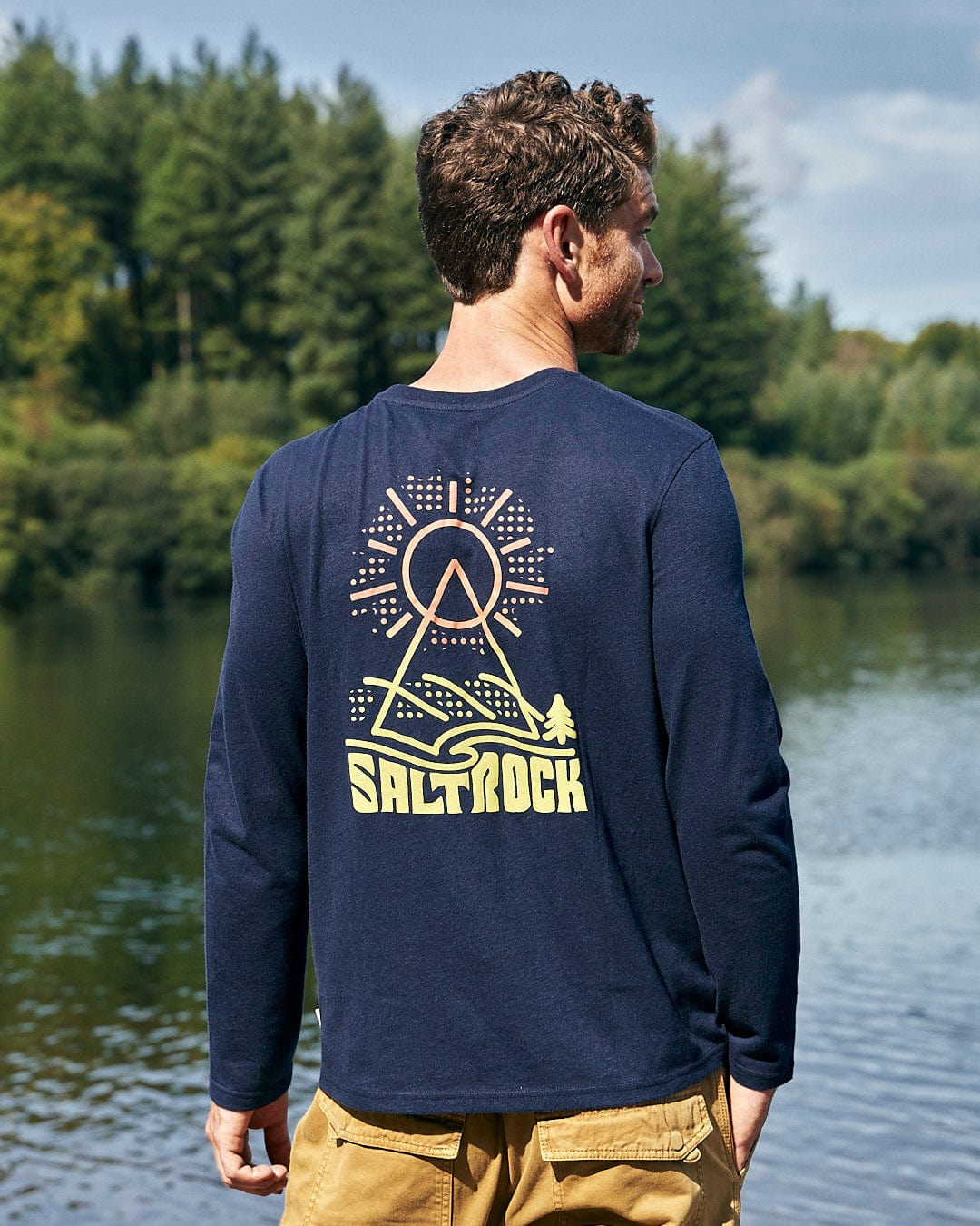 A man wearing a Saltrock Geo Peak - Mens Long Sleeve T-Shirt - Dark Blue looking at the water.