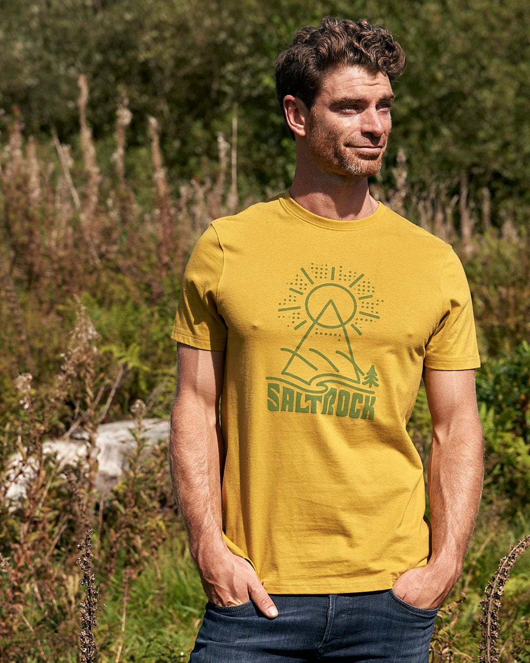 A man standing in a field wearing a Saltrock Geo Peak - Mens Short Sleeve T-Shirt - Yellow.