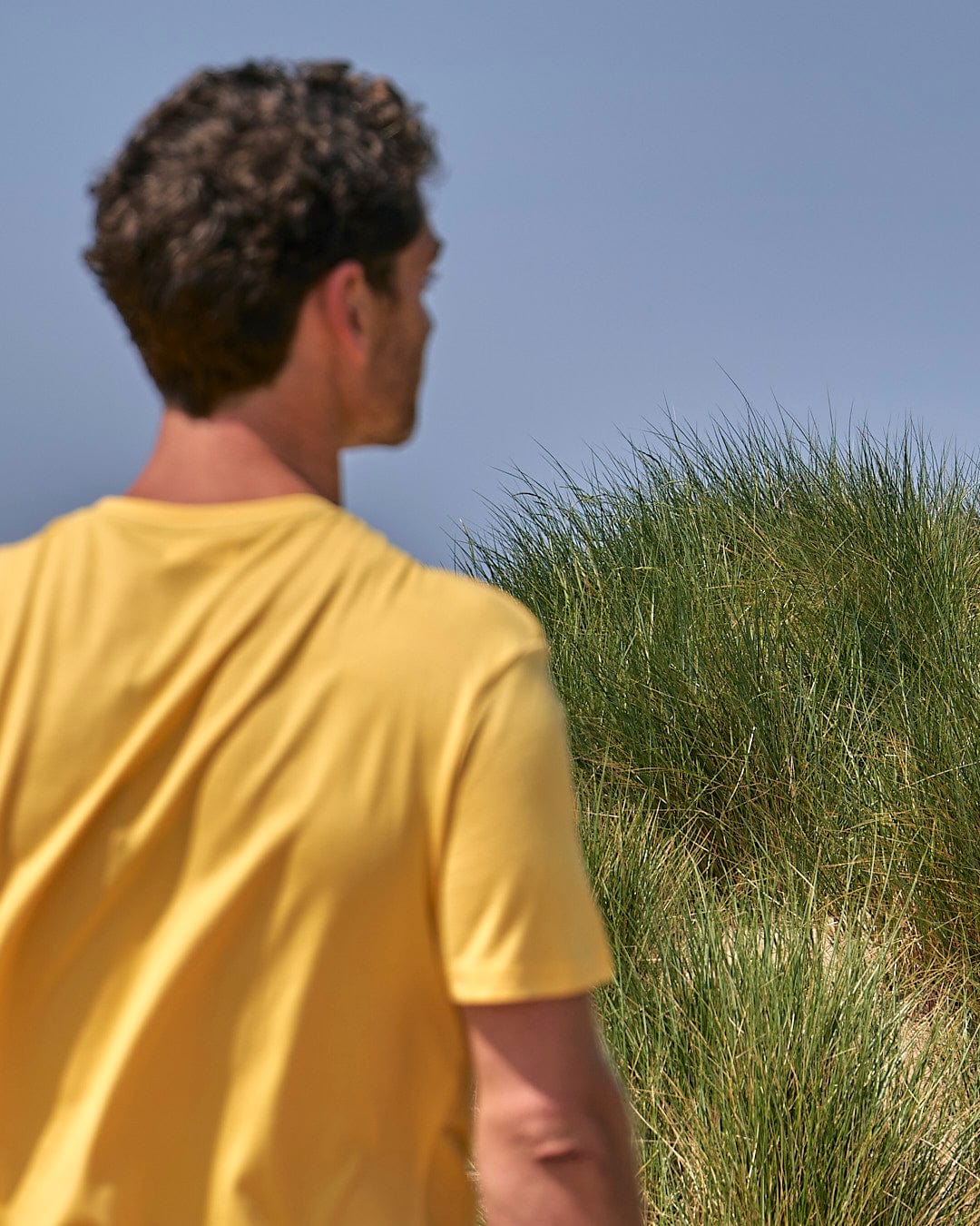 A man is flying a Gradient Hex - Mens Short Sleeve T-Shirt - Yellow by Saltrock on a sand dune.