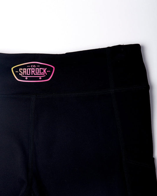 Close-up of a Saltrock black Hardskate kids leggings with the brand logo on a pink and black tag, crafted from super soft fabric.