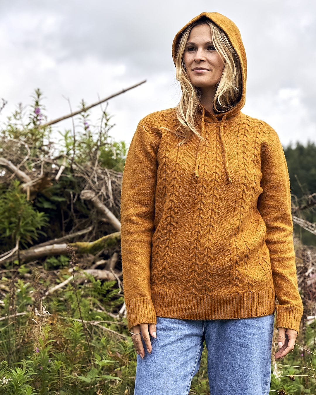 A woman wearing a Saltrock Hele Bay 2 - Womens Knitted Jumper - Yellow hooded sweater standing in a field.