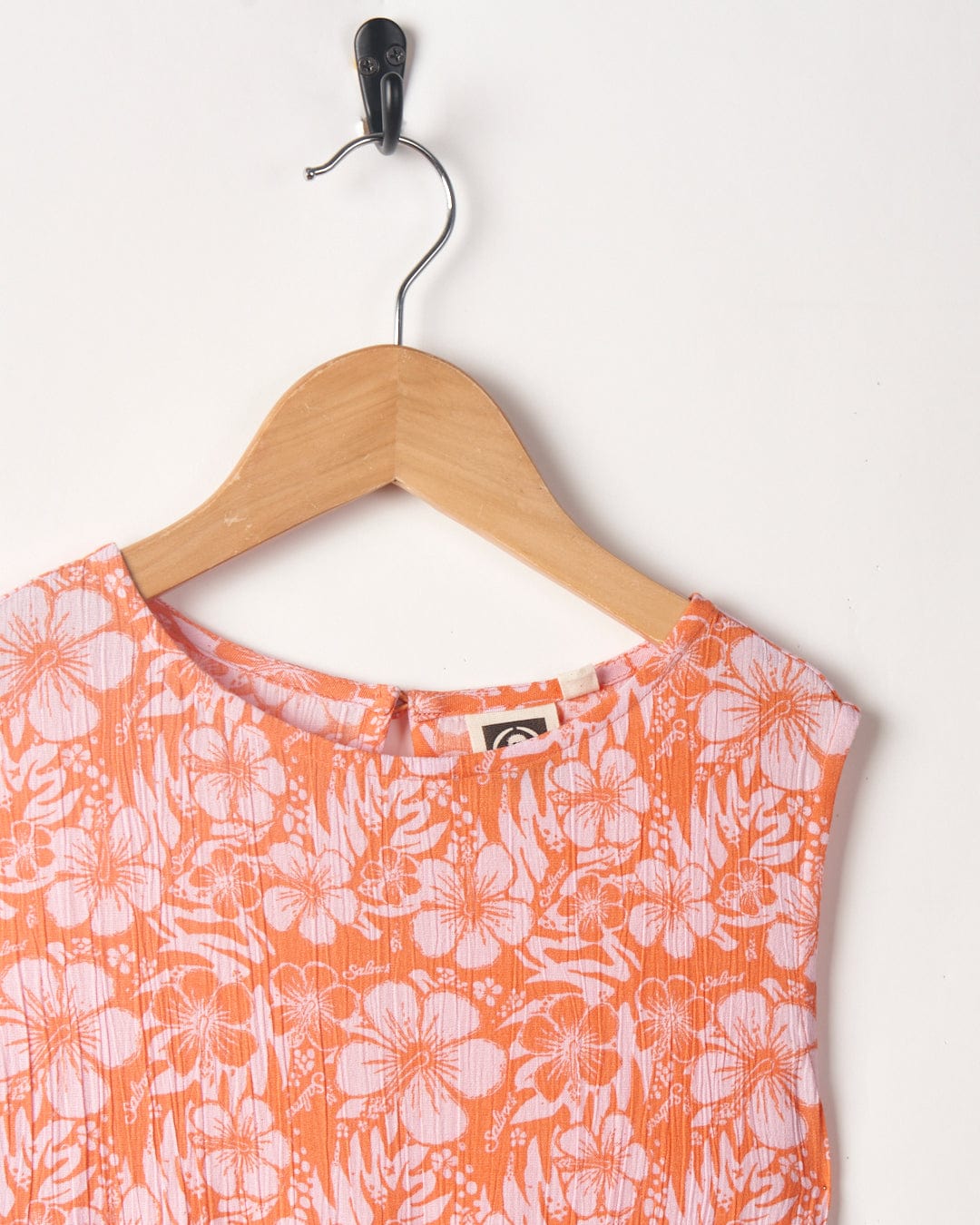 An orange hibiscus flower print Saltrock Kids Playsuit displayed on a wooden hanger against a white background.