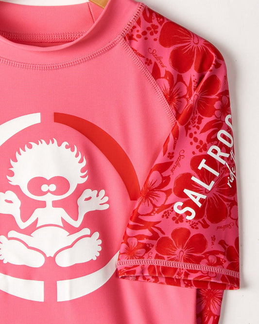 Close-up of a pink Saltrock rash guard featuring a playful white graphic and text "Saltrock Hibiscus" on a floral background.