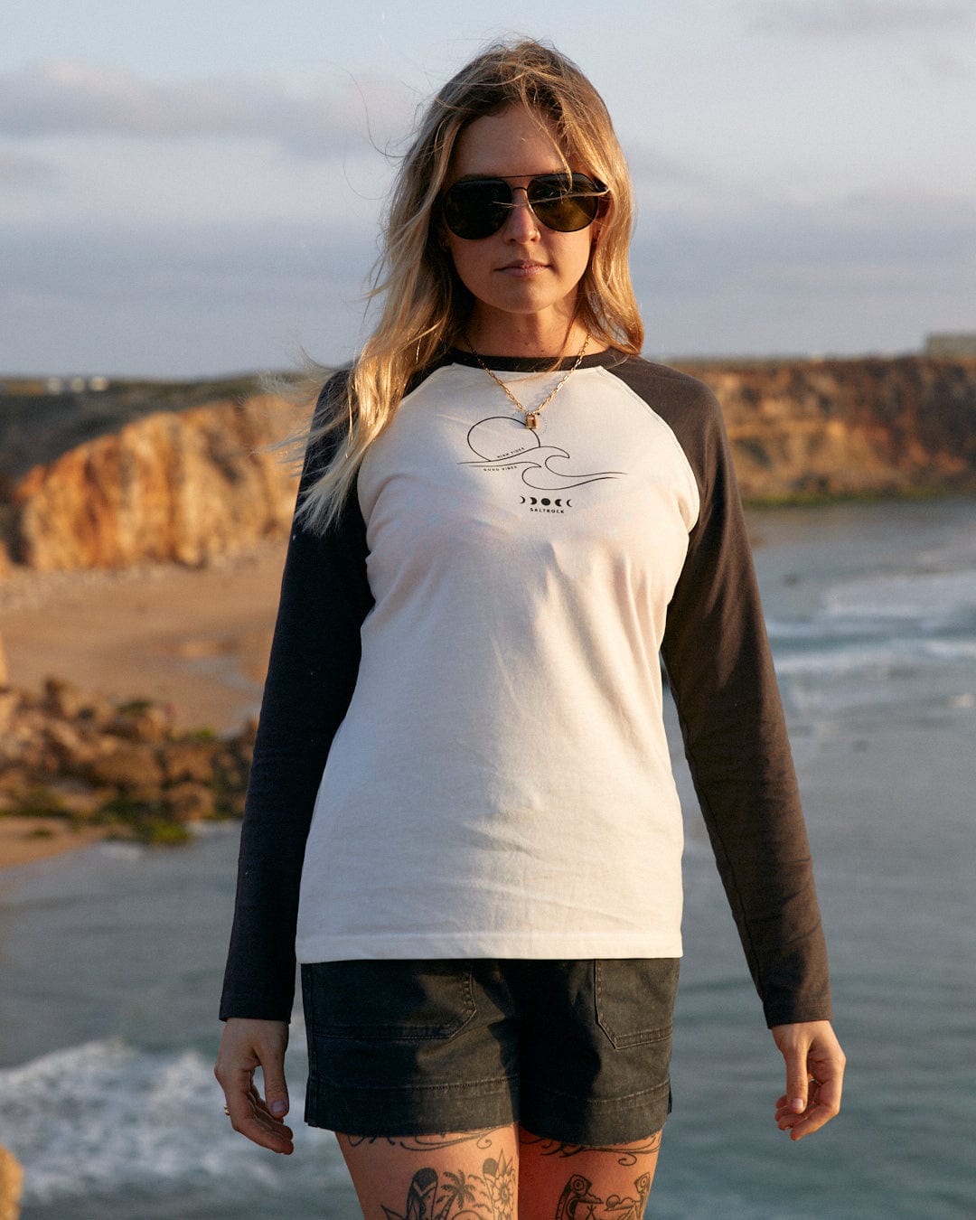 A woman wearing a Saltrock High Tides - Womens Raglan Long Sleeve T-Shirt in White on the beach.