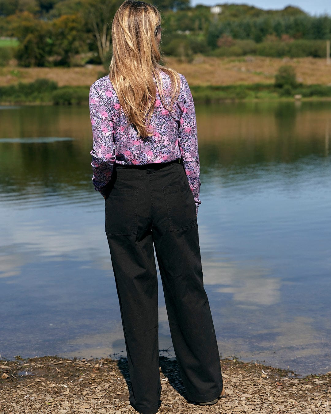 The Saltrock Hilda Twill - Womens Trouser - Black, worn by a woman standing by a body of water.