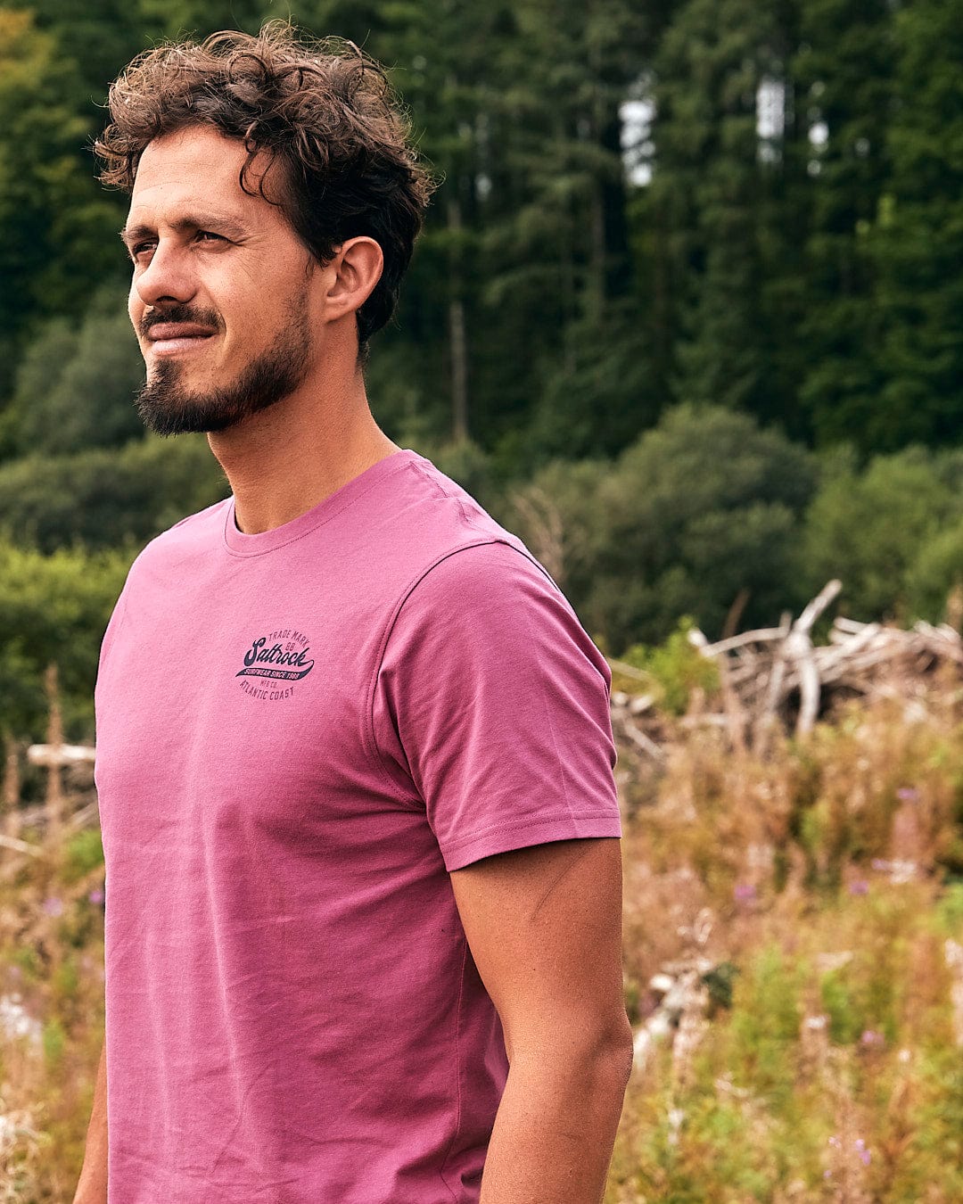 A man wearing a Saltrock - Home Run Mens Short Sleeve T-Shirt - Dark Pink standing in a field.