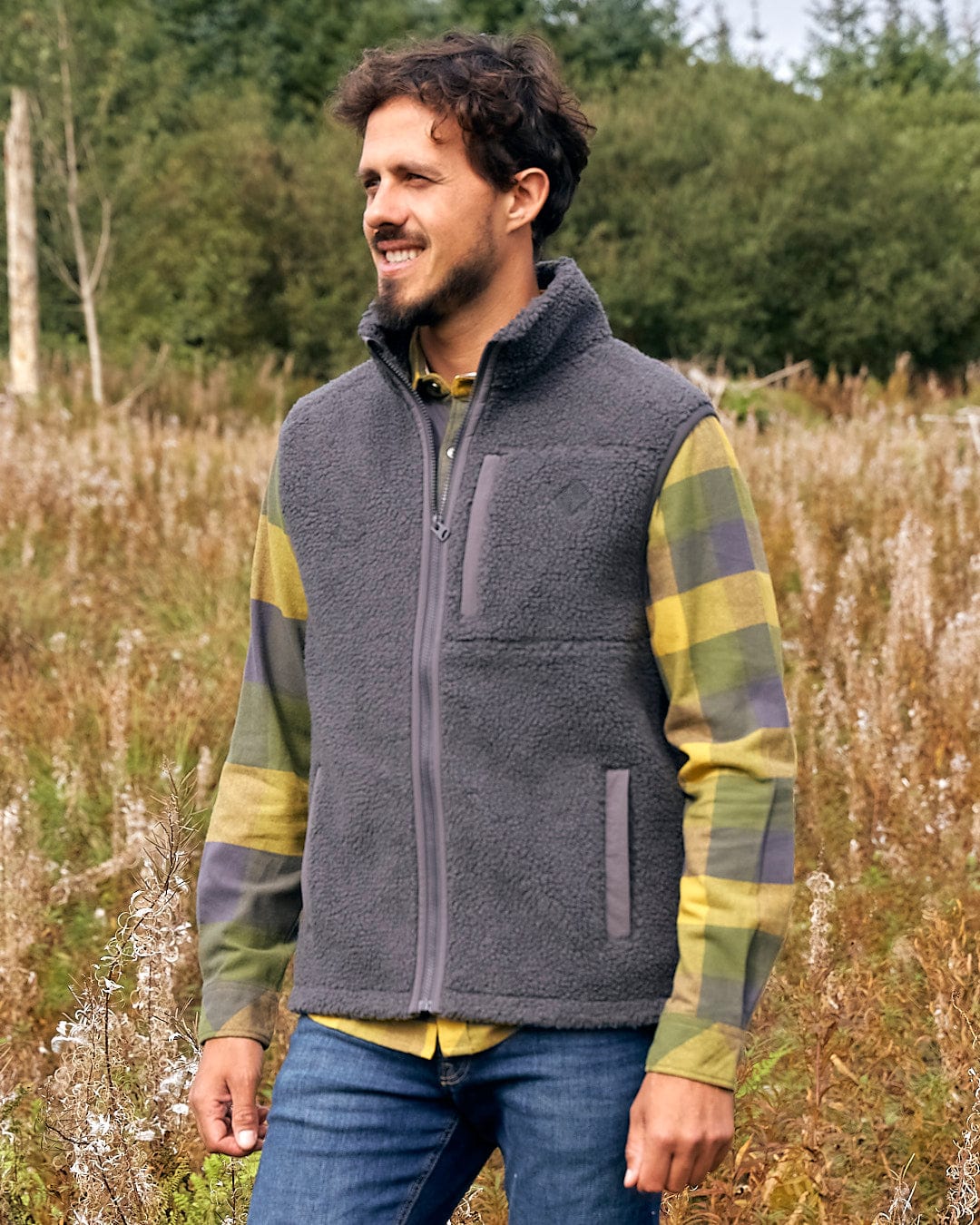 A man is standing in a field wearing a Saltrock Joel - Mens Sherpa Fleece Gilet - Dark Grey.