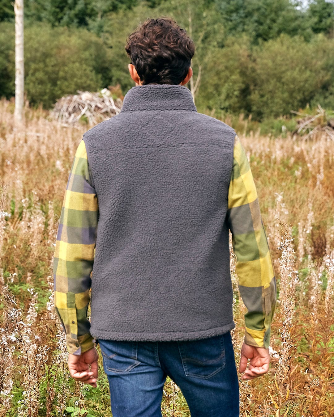 A man is walking through a field in a Saltrock Joel - Mens Sherpa Fleece Gilet - Dark Grey.