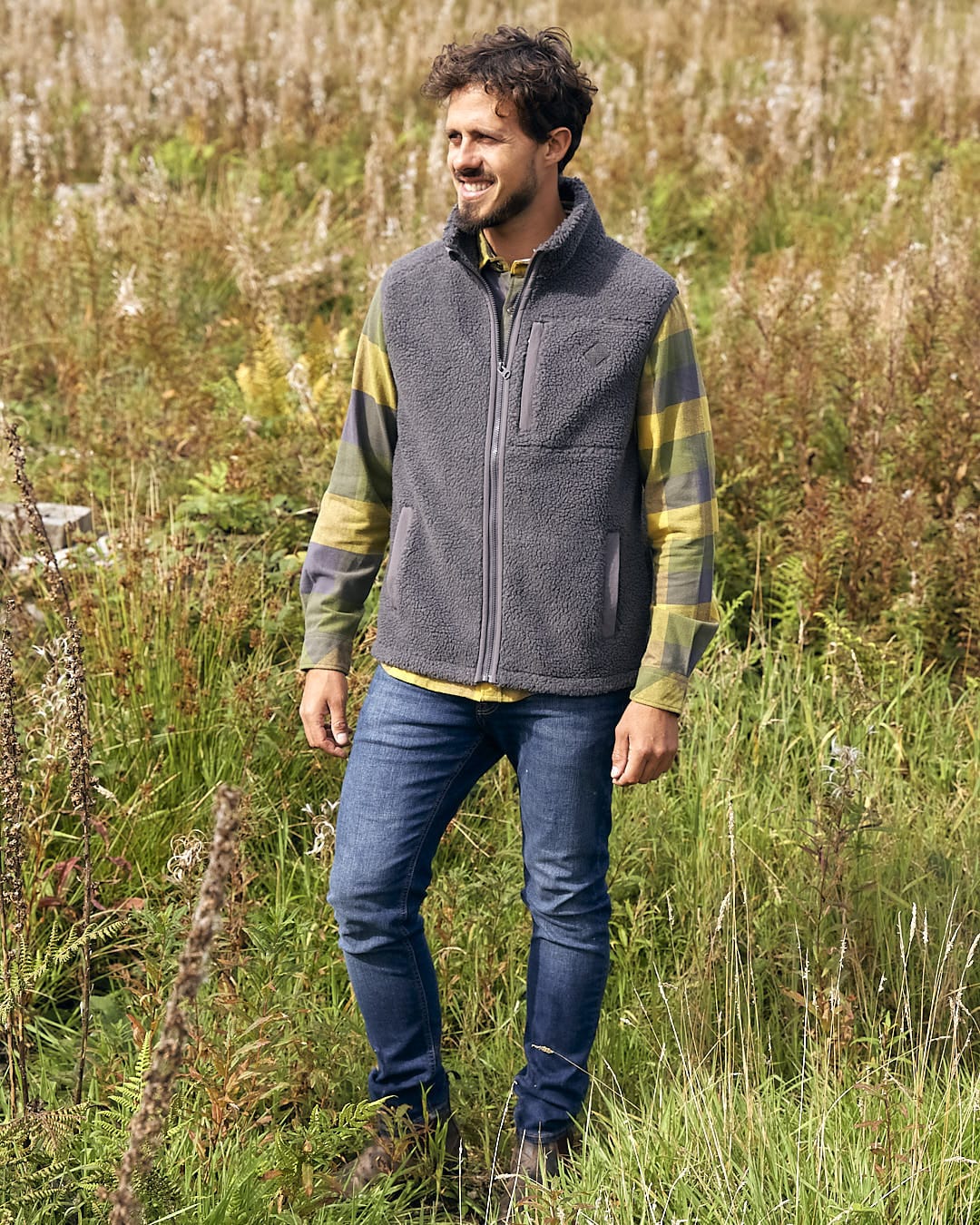 A man standing in a field wearing the Saltrock Joel - Mens Sherpa Fleece Gilet - Dark Grey.