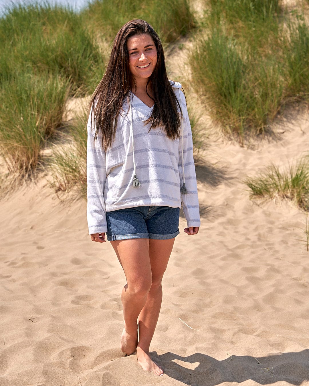 A girl standing on a sand dune wearing the Saltrock Kennedy - Womens Pop Hoodie in Cream and shorts.