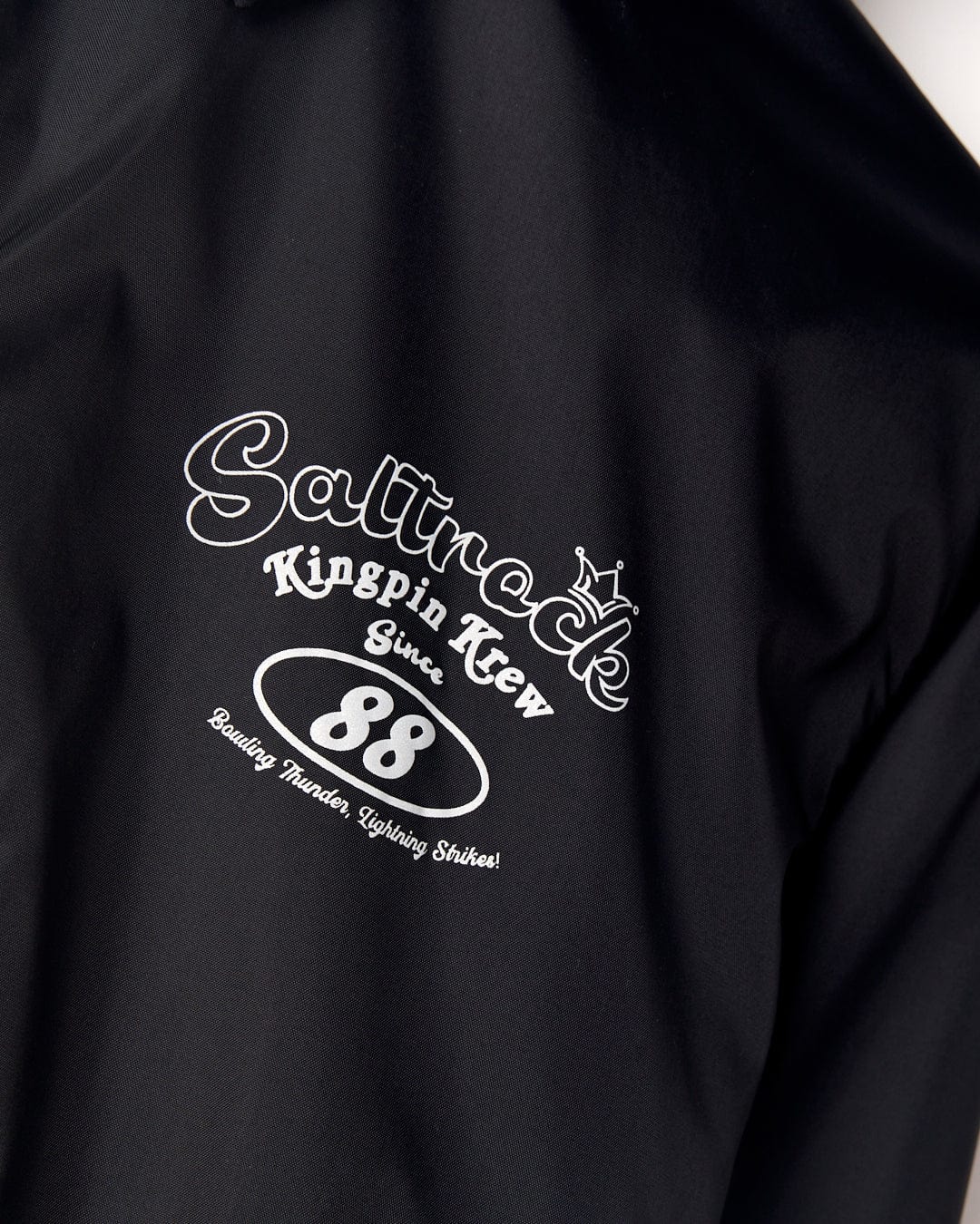 Black fabric with a white printed design saying "Saltrock Kingpin Krew" along with "88" and "summoning thunder lightning strikes!" in an ornate font, featuring a detachable