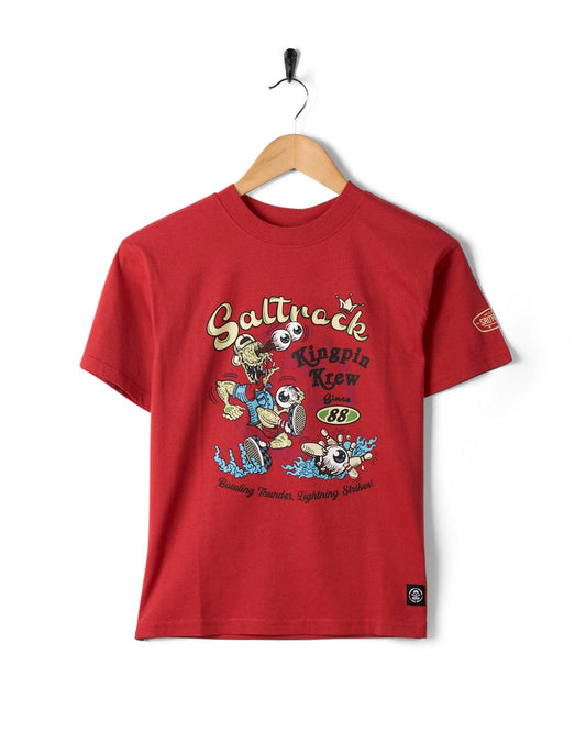 A Saltrock Kingpin Krew - Kids Short Sleeve Glow in the Dark T-Shirt on a hanger featuring a playful cartoon design with text reading "Saltrock Kingpin Krew Since '88" and "Bombing Headen, Lightning Strikes!" This relaxed fit tee is ideal for casual days.