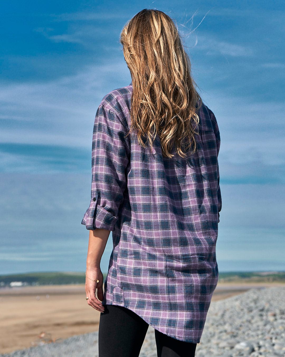 A woman is standing on a beach wearing a Saltrock Kizzie - Womens Check Boyfriend Shirt - Purple.