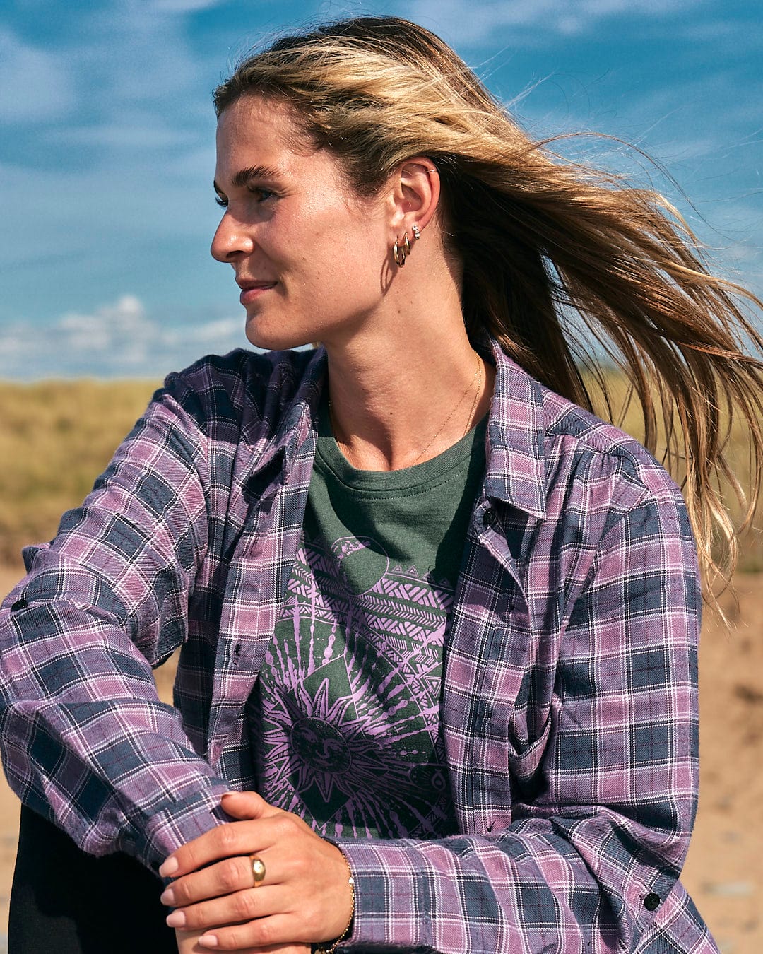 A woman wearing a Saltrock Kizzie - Womens Check Boyfriend Shirt - Purple sitting on the beach.