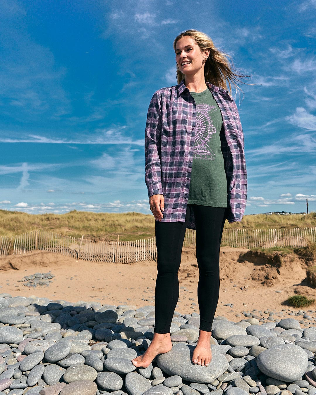 A woman standing on rocks on the beach wearing a Saltrock Kizzie - Womens Check Boyfriend Shirt - Purple.