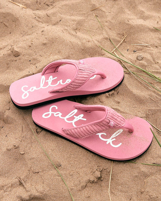 A pair of Saltrock Laguna - Womens Cord Flip Flops - Mid Pink sitting on the sand, providing comfort for beachgoers.