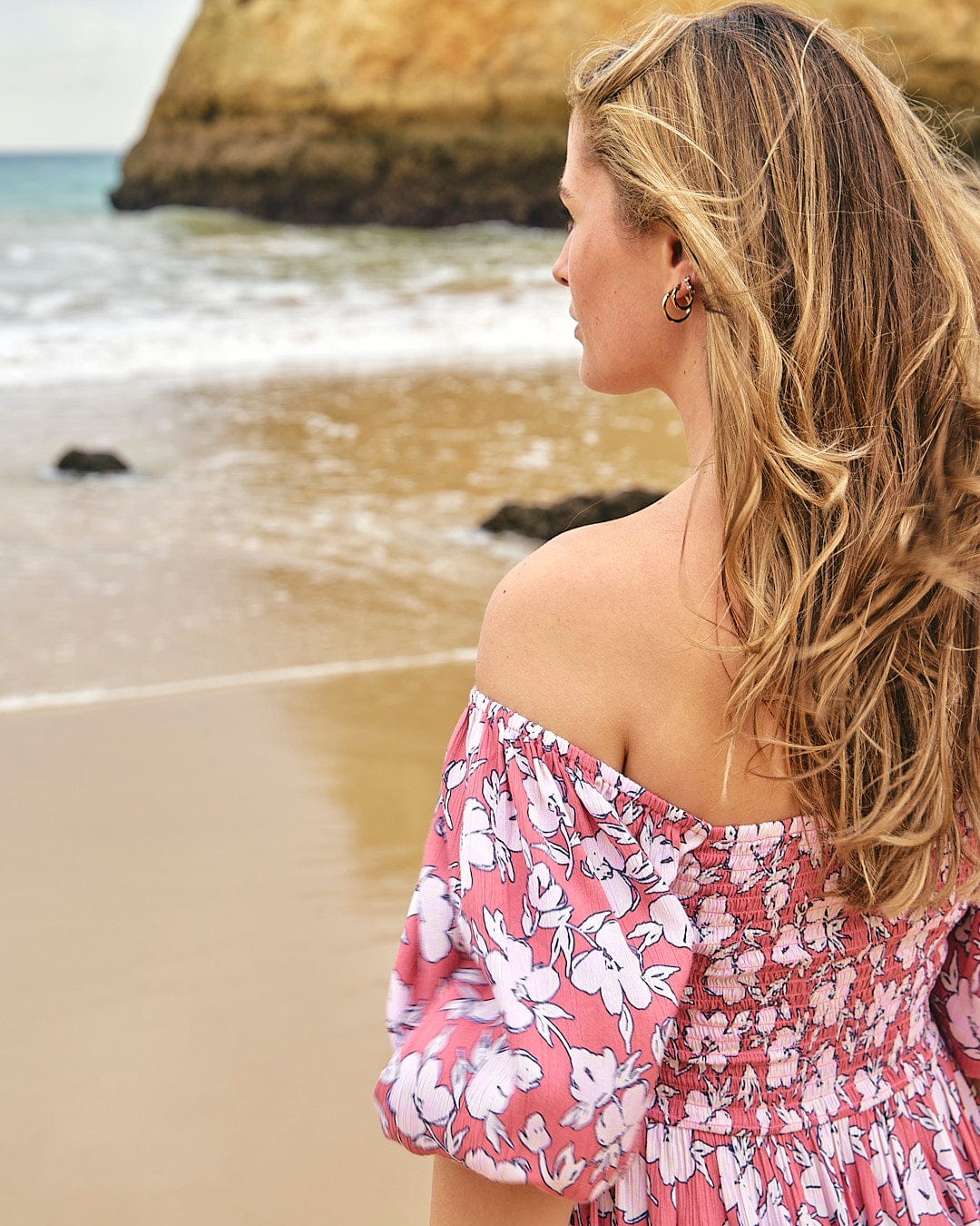 A woman wearing a Saltrock Larran - Womens Shirred Dress - Mid Pink on the beach.