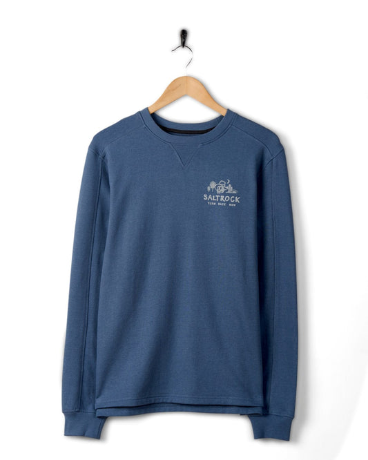 A blue long-sleeve Saltrock sweatshirt with a "Last Stop Motel" logo on the chest, hanging on a wall-mounted hook against a white background.
