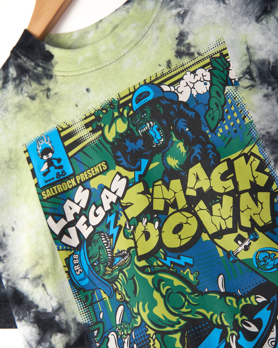 Close-up of a Saltrock Las Vegas Smackdown - Kids Glow in the Dark T-Shirt - Multi, featuring cartoon characters and vibrant text. The shirt showcases a tie-dye pattern in black, white, and green, enhanced with glow in the dark graphics for an extra pop.