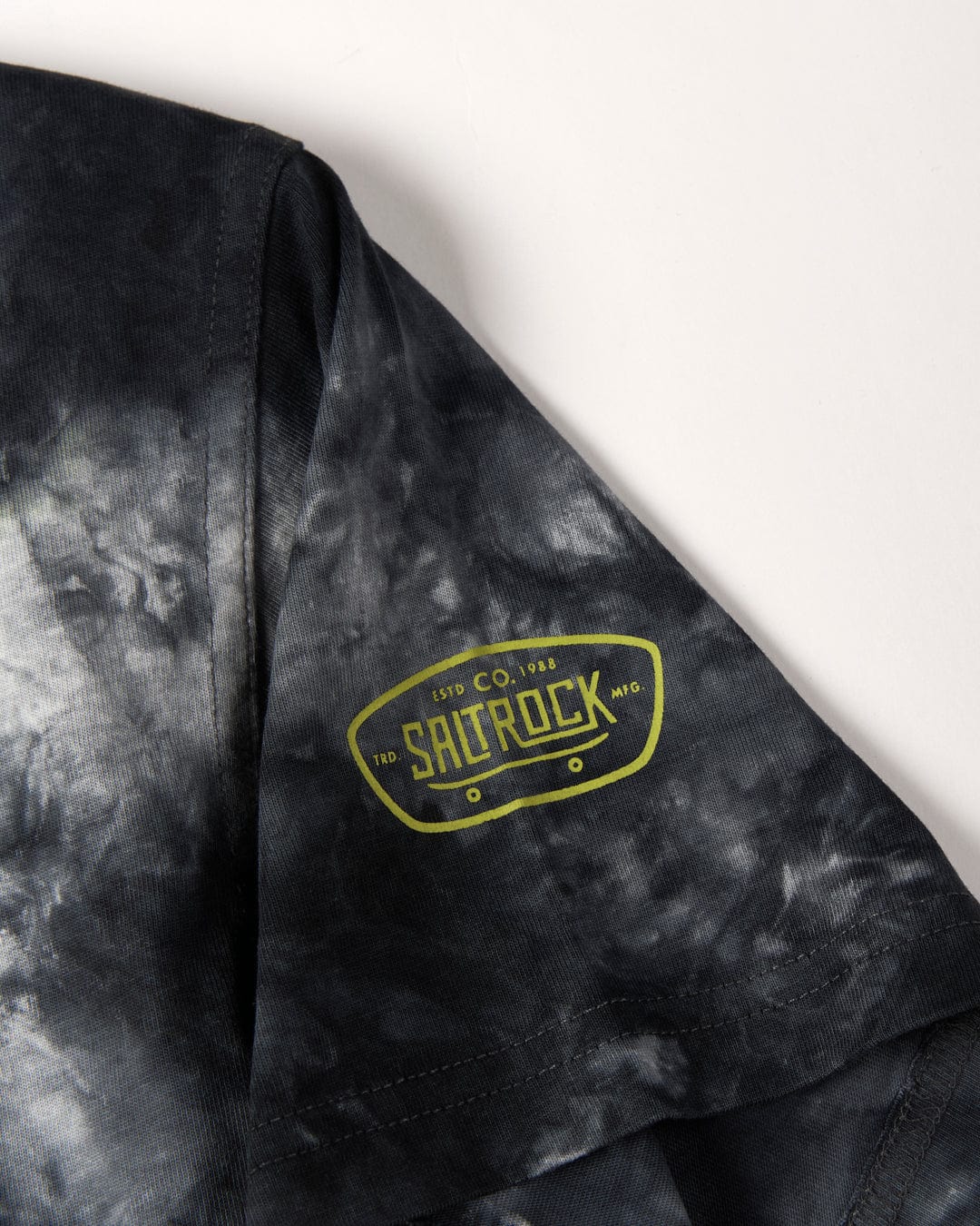 Close-up of a black and gray tie-dye pattern fabric featuring a green "SaltRock" logo, reminiscent of Las Vegas Smackdown - Kids Glow in the Dark T-Shirt - Multi by Saltrock skateboard aesthetics.